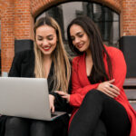 Two young friends using a laptop outdoors.