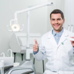 dentist holding toothpaste and showing thumb up in dental clinic