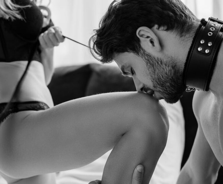A man wearing a leather collar kneels and kisses a woman’s leg, symbolizing trust, control, and connection, illustrating the essence of a BDSM Guide for Beginners.