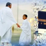 A father and son dressed in white Ihram garments walking together towards the Holy Kaaba in Makkah, surrounded by pilgrims