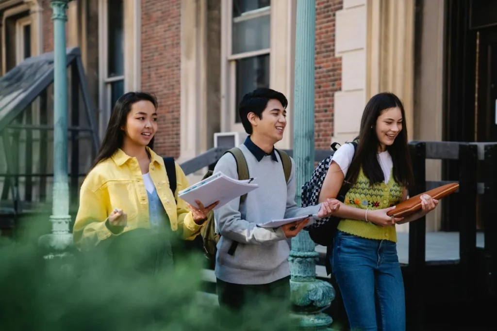 A photograph of three international students walking and talking on a UK university campus, illustrating the demographic that utilizes assignment help for international students in the UK to succeed academically.