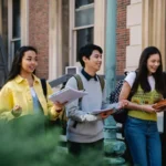 A photograph of three international students walking and talking on a UK university campus, illustrating the demographic that utilizes assignment help for international students in the UK to succeed academically.