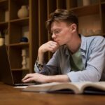 A young man sitting at a desk at home, focused on a laptop screen while studying for his NREMT cognitive exam.