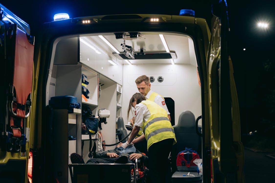 Two paramedics seated inside an ambulance, wearing uniforms and preparing equipment while awaiting or transporting during an emergency response