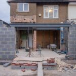 Rear view of a residential property undergoing a house extension London, featuring a large steel support beam, exposed breeze block walls, and construction equipment.
