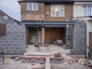 Rear view of a residential property undergoing a house extension London, featuring a large steel support beam, exposed breeze block walls, and construction equipment.