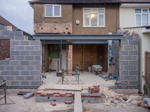 Rear view of a residential property undergoing a house extension London, featuring a large steel support beam, exposed breeze block walls, and construction equipment.