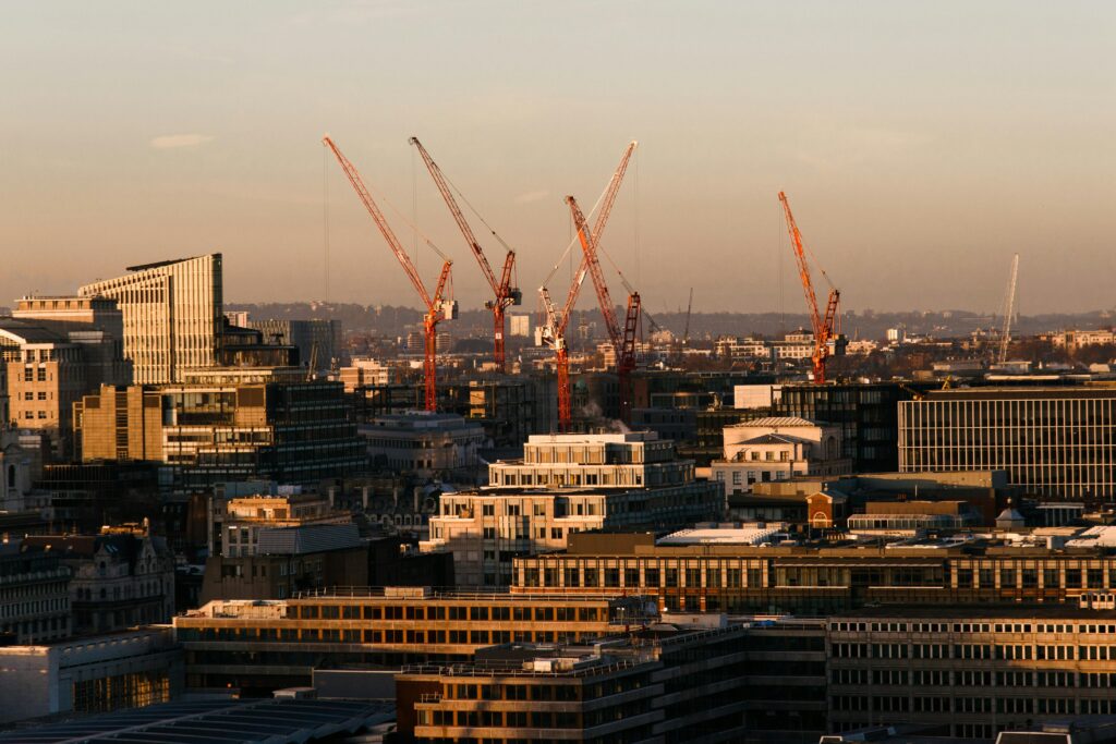 Panoramic view of construction cranes over a city skyline at sunset illustrating the work of top construction companies UK.