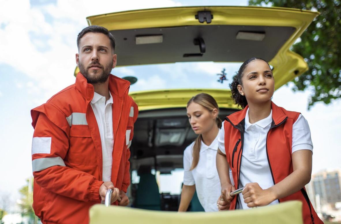Two EMTs look around for environmental hazards while rolling out a stretcher in a parking lot