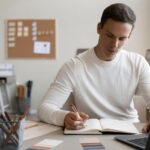 A student sitting at a desk taking notes while studying for the NREMT exam