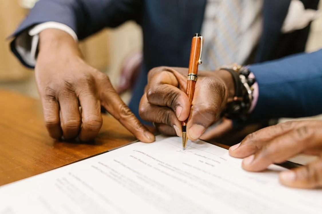 a person directing another person where to sign the form placed on a wooden table