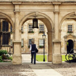 A student walking through a historic stone archway at a traditional British campus, illustrating the successful placement services provided by UK University Admission Consultants.
