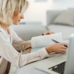 Woman studying NREMT exam questions at home using a laptop and textbook