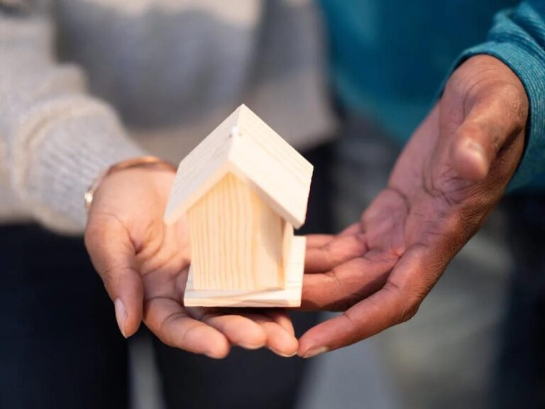 two people holding a miniature model of a wooden house together