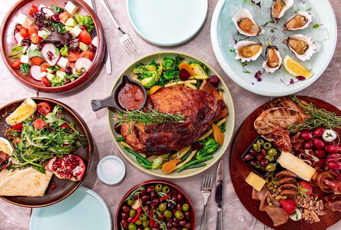 Overhead view of a gourmet dining table spread with roasted meats, fresh salads, seafood, fruits, and cheese