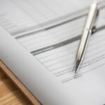 an empty form on a clipboard placed on a desk with a silver pen on it