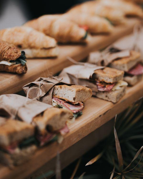 Several wrapped deli sandwiches and croissants arranged on wooden serving boards, with fillings of meat and greens visible.