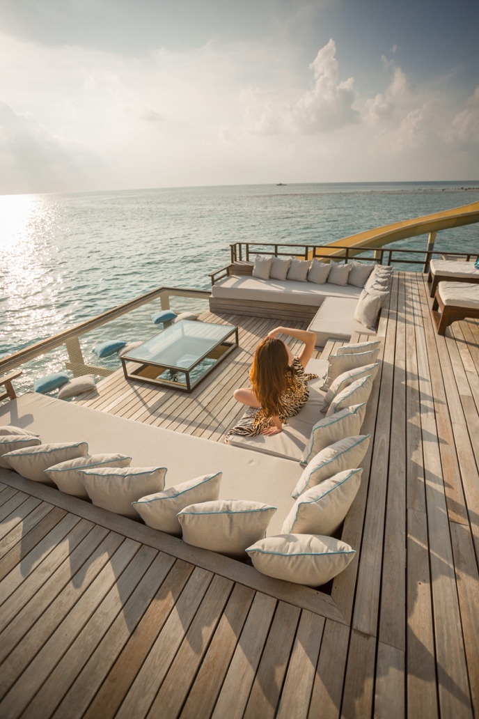 A woman relaxing comfortably on a luxurious, sun-drenched outdoor sofa on the deck of a yacht, surrounded by immaculate, spotless cushions and polished marine accents.