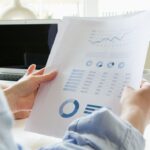 Person holding printed papers showing financial data for insurance analysis