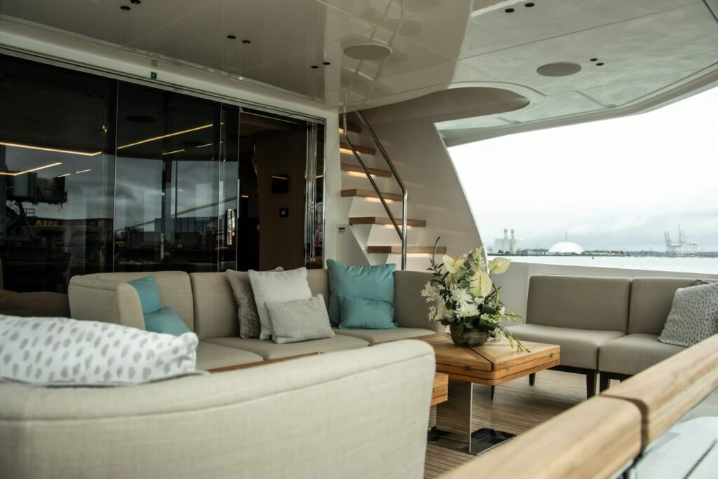 The pristine outdoor lounging deck of a luxury yacht featuring spotless cream cushions, polished accents, and immaculate teak detailing under a sun-drenched sky