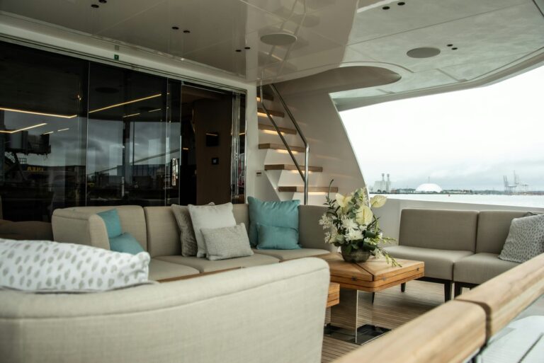 The pristine outdoor lounging deck of a luxury yacht featuring spotless cream cushions, polished accents, and immaculate teak detailing under a sun-drenched sky