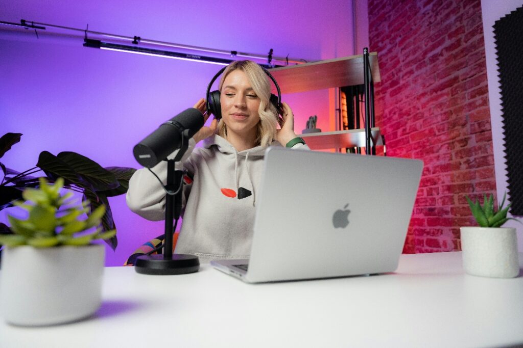 Female content creator wearing headphones recording audio with a microphone and laptop in a modern studio setup