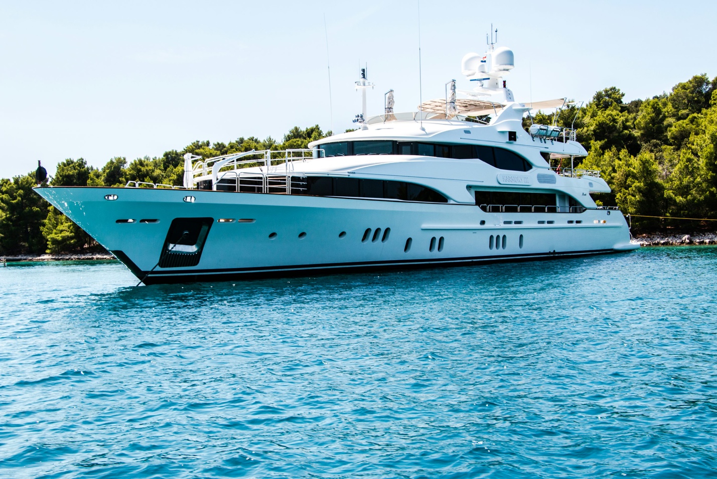 A broadside profile view of a luxury motor yacht resting in clear turquoise waters