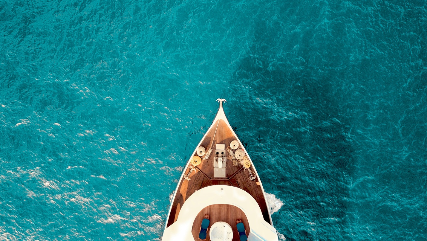 An aerial top-down view of a large luxury superyacht anchored in crystal-clear, turquoise water near the Florida coast