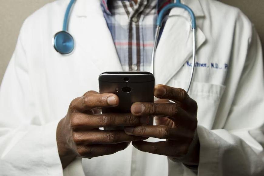 An image of a doctor wearing a stethoscope using his phone