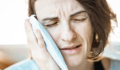 Woman applying a cold compress to her cheek for relief from toothache pain