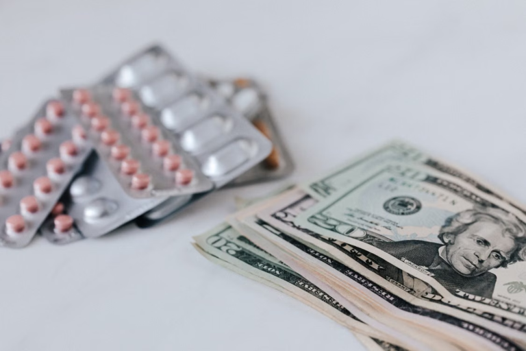 Blister packs of pills placed beside a stack of U.S. dollar bills on a white surface.