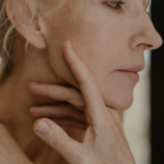 older woman examining her skin while reflecting visible signs associated with the biological aging process