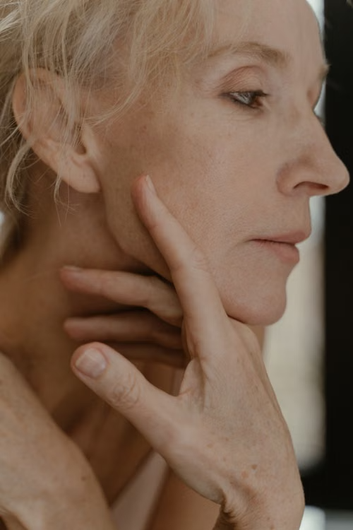 older woman examining her skin while reflecting visible signs associated with the biological aging process