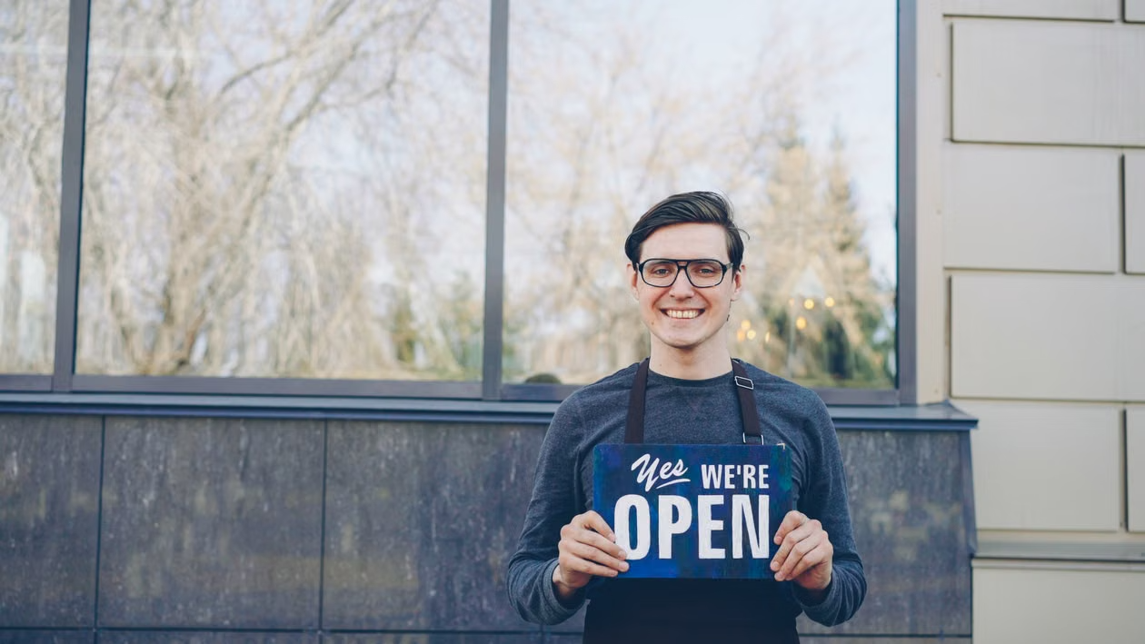 business owner holding an open sign outdoors