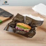 Custom printed black food wrapping paper with a sandwich, branded burger illustrations, and food packaging containers by Print On Papers.