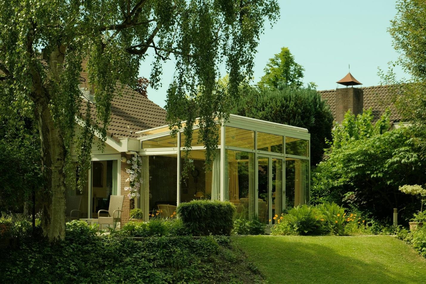 A modern enclosed sunroom attached to a house, surrounded by trees